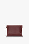 A rectangular maroon grained leather clutch bag with a detachable strap, against a white background, is the Victoria Beckham Jumbo Chain Pouch Bag In Bordeaux.