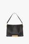 A Victoria Beckham Jumbo Chain Pouch Bag In Black Leather with a single shoulder strap and a striking gold-tone chain detail at the bottom center.