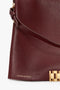 Close-up of a maroon grained leather handbag with a gold clasp and the label "Victoria Beckham" embossed in gold lettering, featuring a detachable strap. The product is the Jumbo Chain Pouch Bag In Bordeaux by Victoria Beckham.