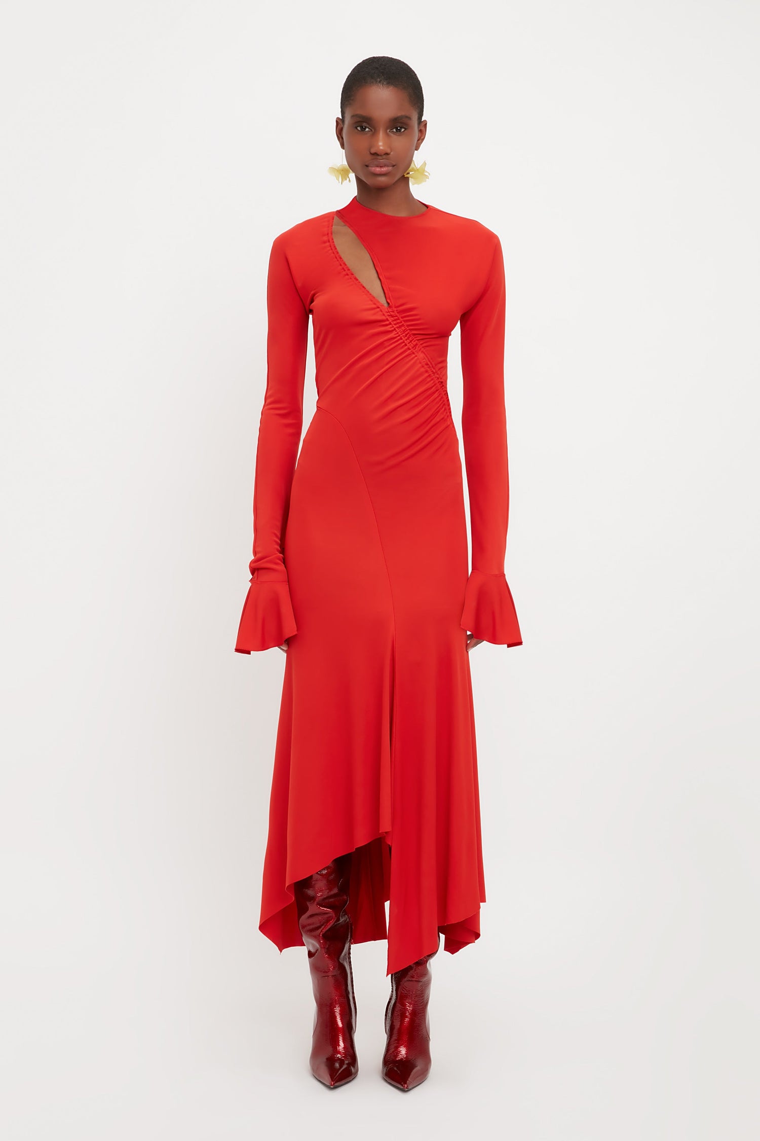 Model wearing a red midi dress from luxury fashion designer Victoria Beckham. This red body con dress is made from jersey and has a slash front detail. With a gathered waist and asymmetric hem and long sleeves.
