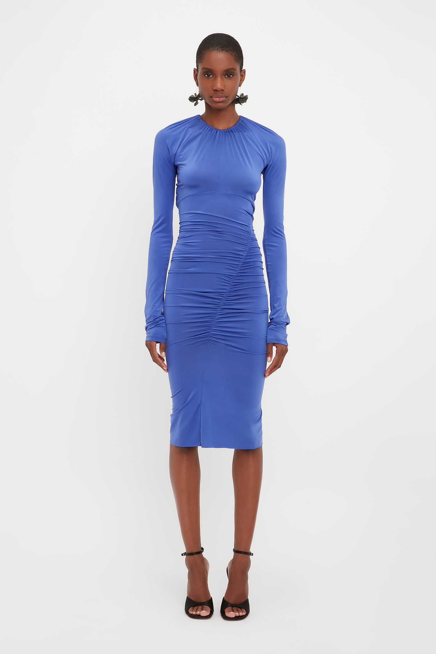 Model wears the Victoria Beckham longsleeve fitted dress in blue. This gathered detail dress comes in a midi length with long sleeves and tie back detailing.
