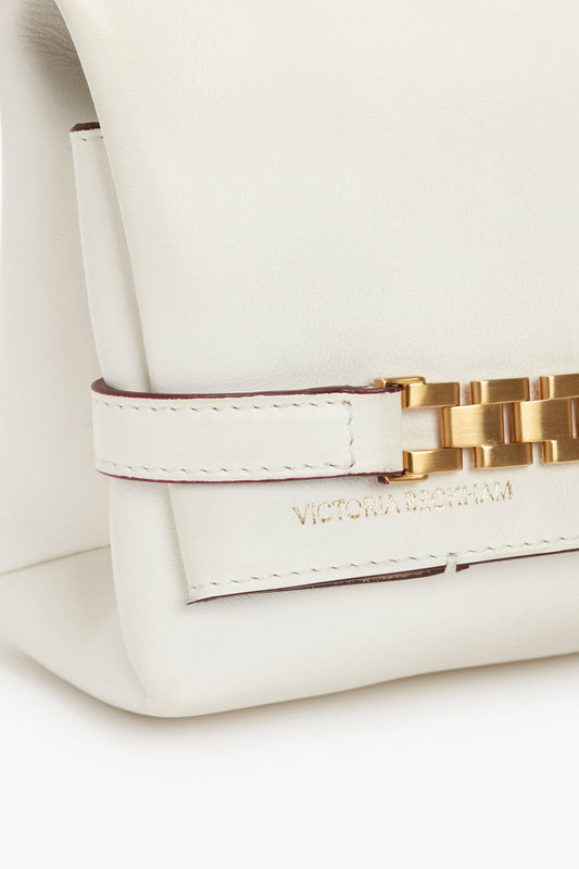 A close-up of a Mini Chain Pouch Bag With Long Strap In White Leather with a gold clasp, featuring a removable strap and the name "Victoria Beckham" embossed on it.