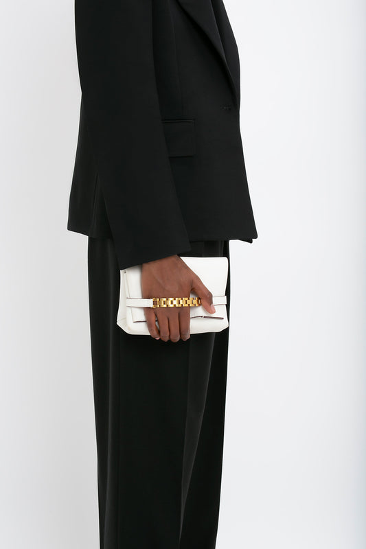 Person in a black suit holding a Victoria Beckham Mini Chain Pouch Bag With Long Strap In White Leather against a plain white background.