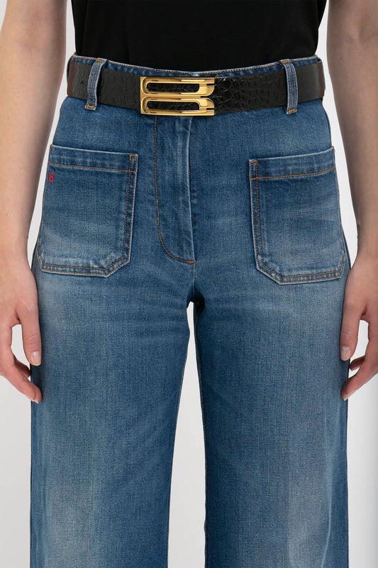 A person wearing blue denim jeans with a Victoria Beckham Jumbo Frame Belt In Chocolate Croc-Effect Leather, featuring two gold buckles for a touch of contemporary styling.